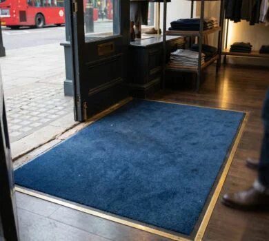 a well-maintained blue entrance mat positioned immediately inside the doorway of an upscale boutique on a London high street