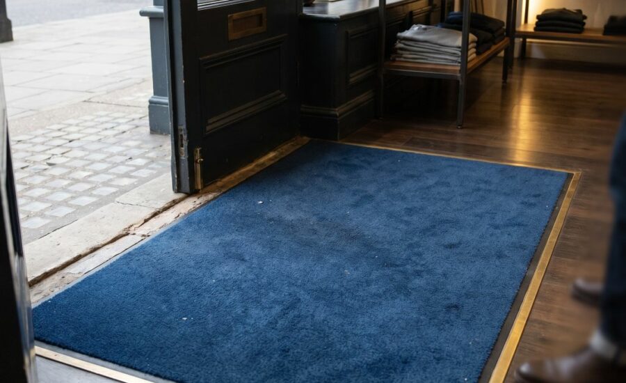 a well-maintained blue entrance mat positioned immediately inside the doorway of an upscale boutique on a London high street